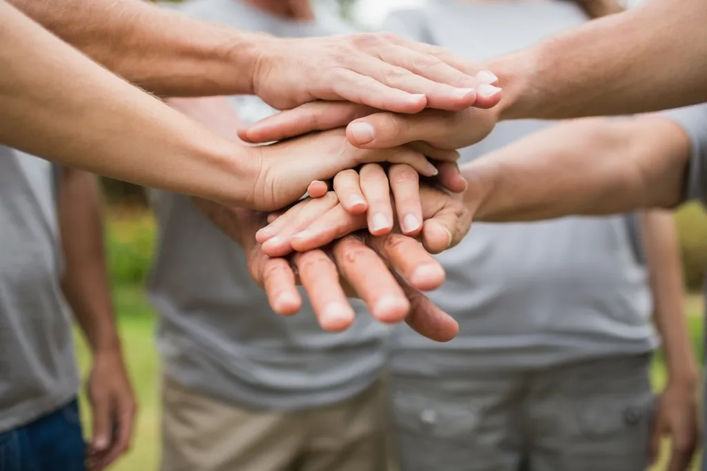 Close-up of several people's hands stacked together in a circle outdoors, neutral skin tones, teamwork mood